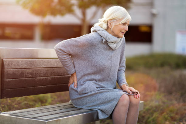 Old lady on a park bench holding lower back in pain