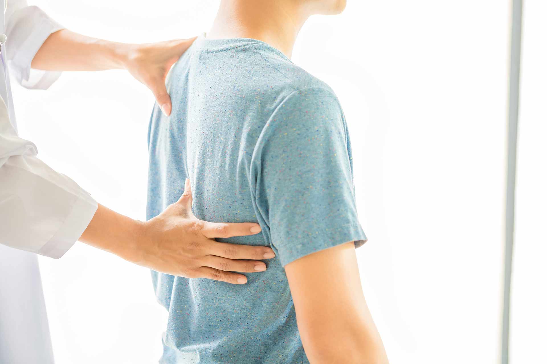 Close up image of a Physiotherapist's hands working on the back of a seated patient wearing a blue shirt